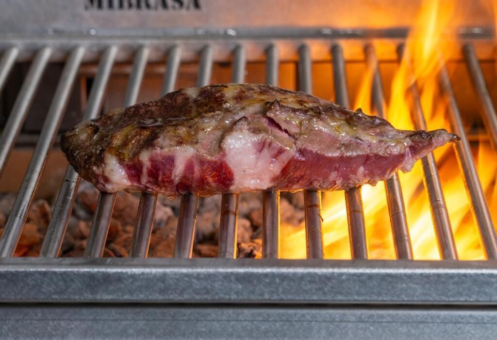 A steak being grilled on a metal grate over an open flame.