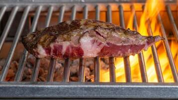 A steak being grilled on a metal grate over an open flame.