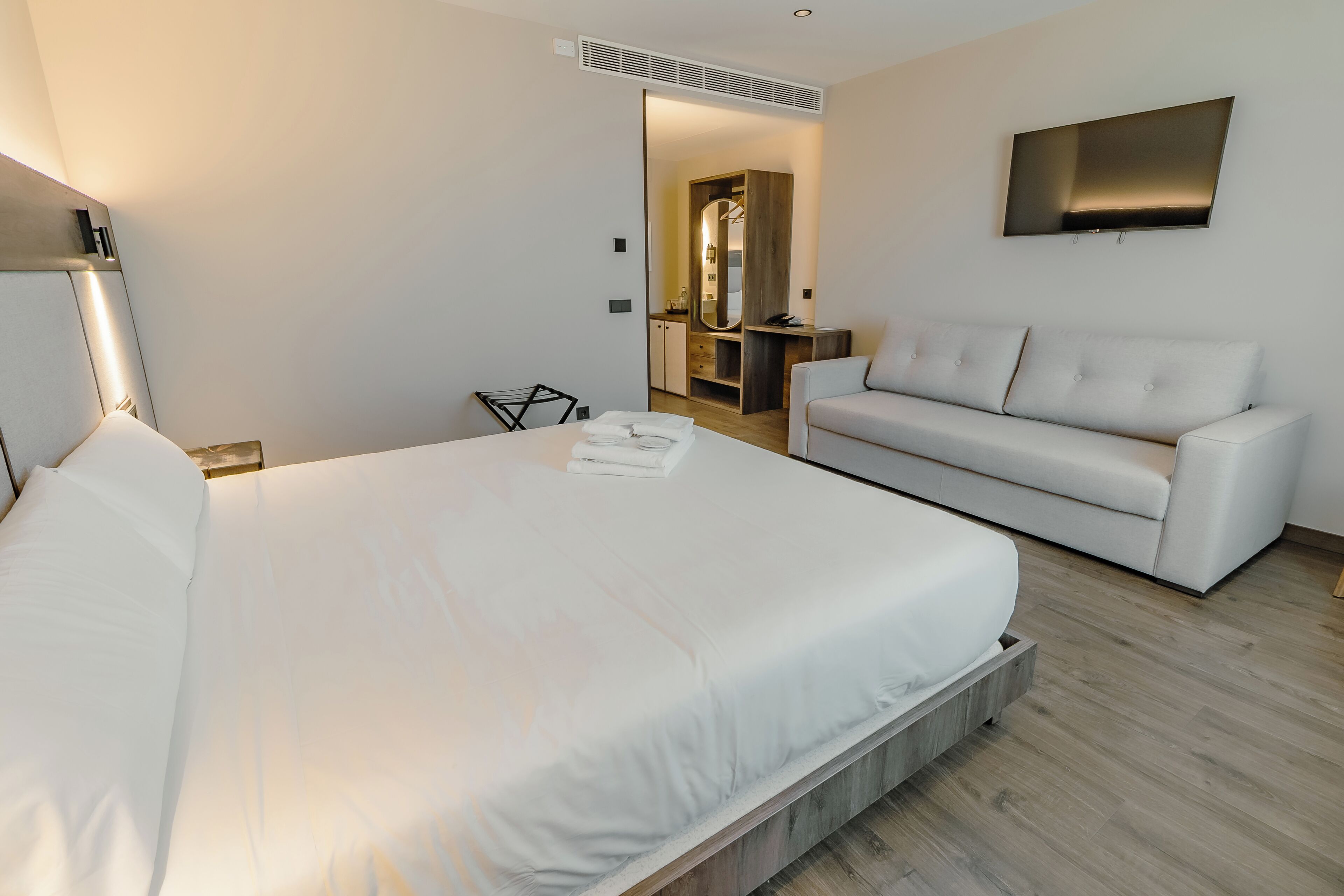 Una habitación de hotel moderna con una cama grande, un sofá, un televisor y un vestidor.