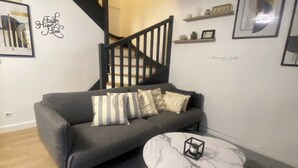 A living room with a grey sofa, a round coffee table, a staircase, and wall decorations.