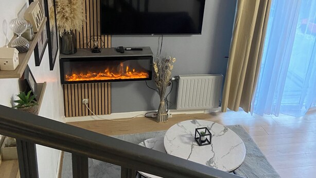 A modern living room with a flat-screen TV mounted on the wall, a fireplace, and a small round table with a decorative item.