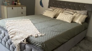 A bedroom with a tufted headboard, a grey bedspread, and a decorative wall with French text and a feather design.