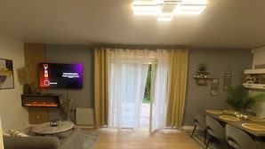 A modern living room with a flat-screen TV, a fireplace, a sofa, and a dining area with a table and chairs.