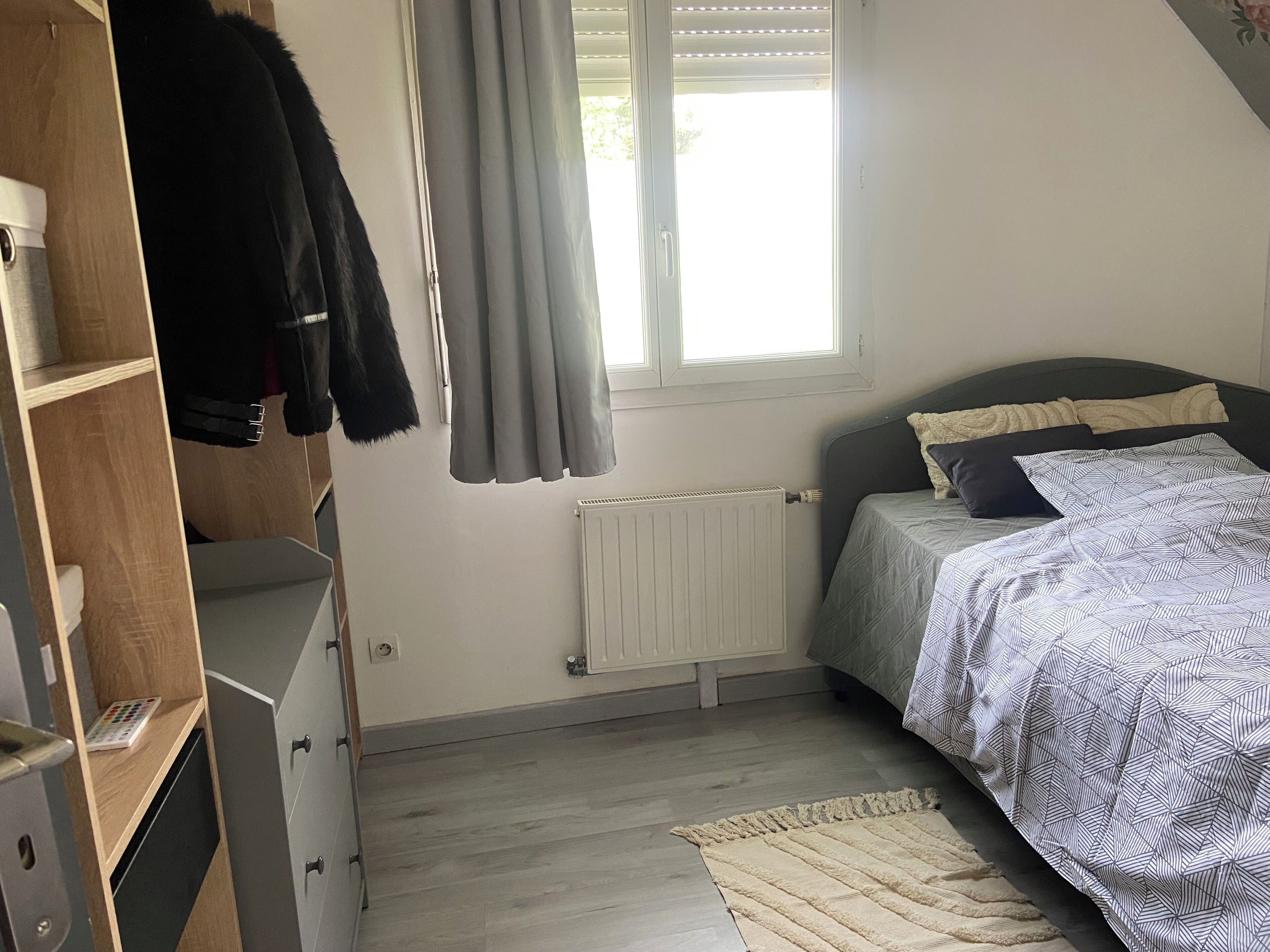 A bedroom with a bed, a wardrobe, a radiator, and a window with curtains.
