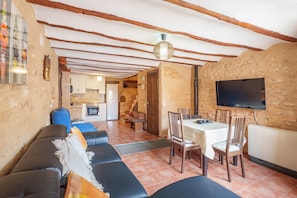Un salon confortable avec un canapé, une table à manger et des chaises, une cuisine en arrière-plan et un téléviseur fixé au mur.