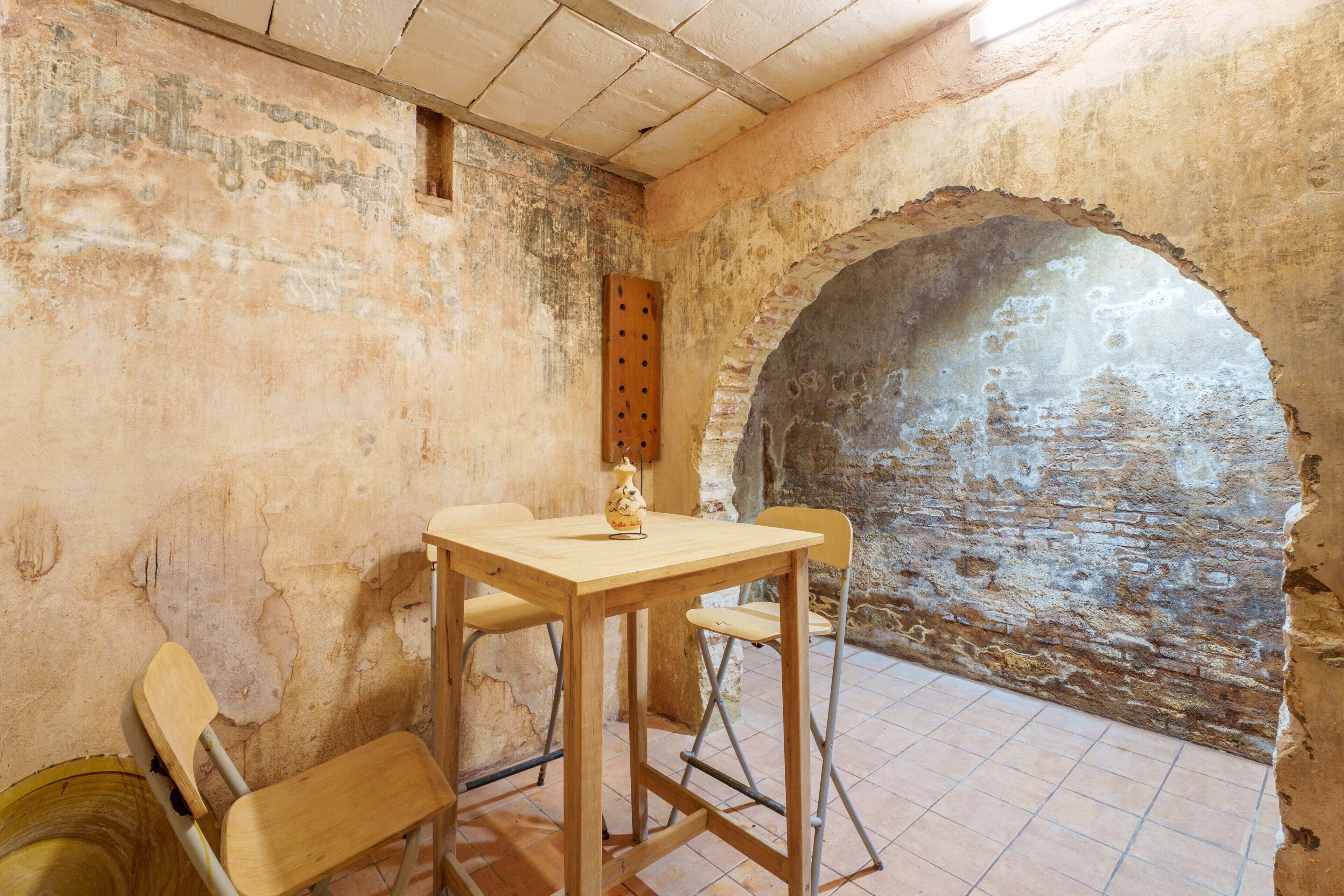A room with a rustic stone wall, a wooden table with two chairs, and a small wooden stool.