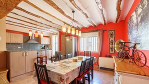 A dining area with a table set for six, wooden chairs, a chandelier, and a kitchen in the background.