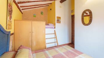 A bedroom with a bed, wooden wardrobe, ladder, and a wall-mounted mirror.