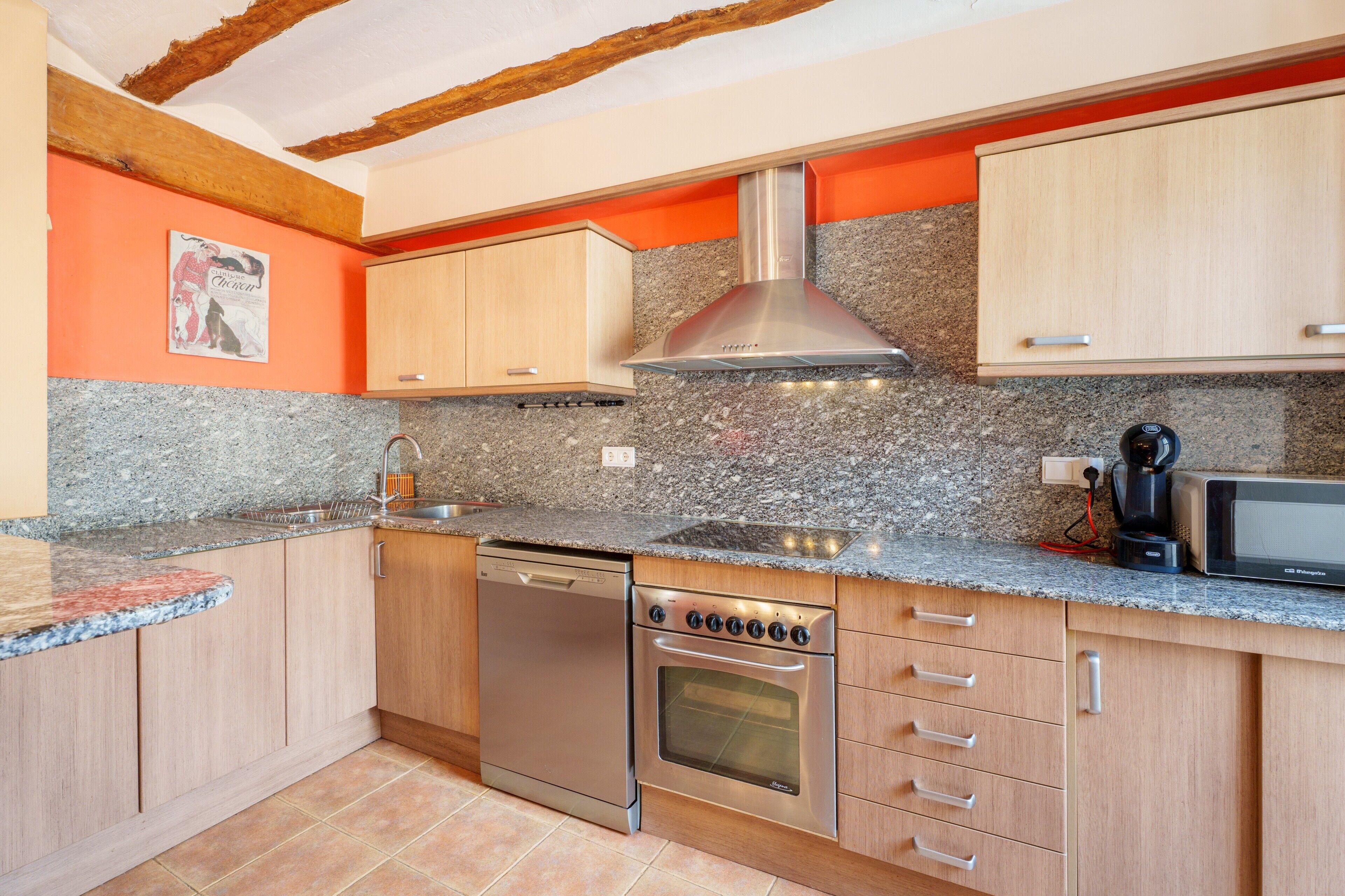 A kitchen with granite countertops, stainless steel appliances, wooden cabinets, and a red accent wall.