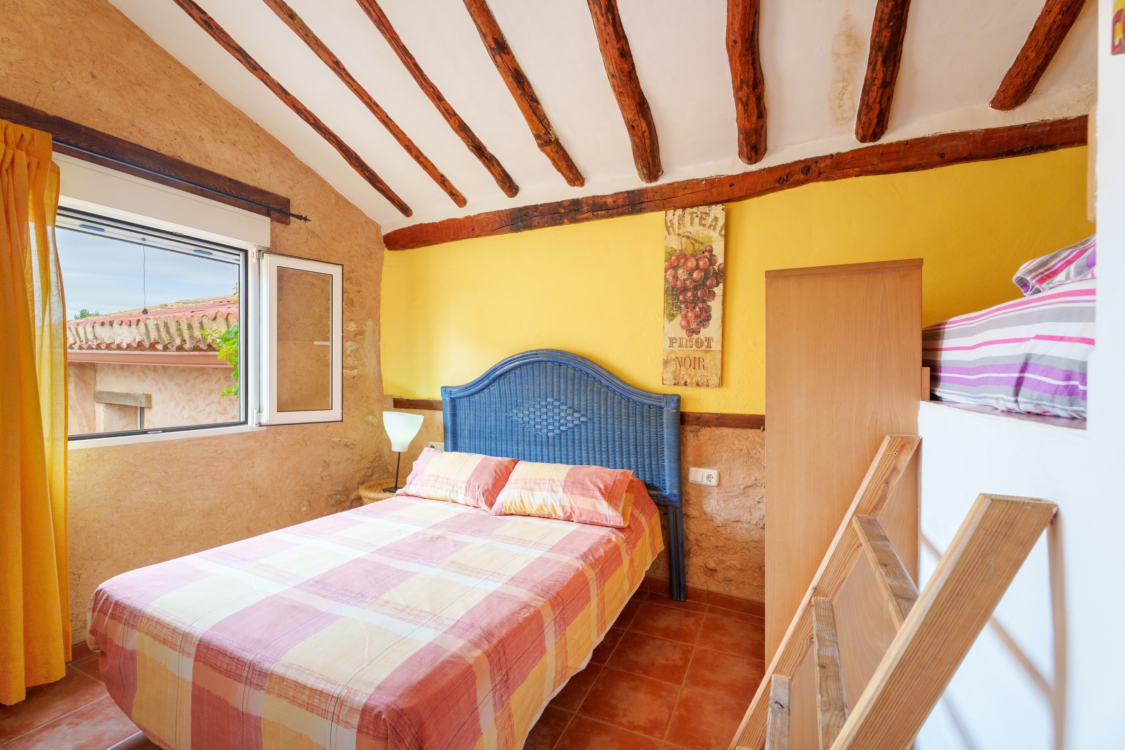 Un dormitorio con cama, vigas de madera, una ventana con cortinas y un cartel en la pared.