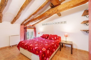 Une chambre avec un plafond en bois, un lit recouvert d’une courtepointe à motifs rouges, deux lampes de chevet et un radiateur.