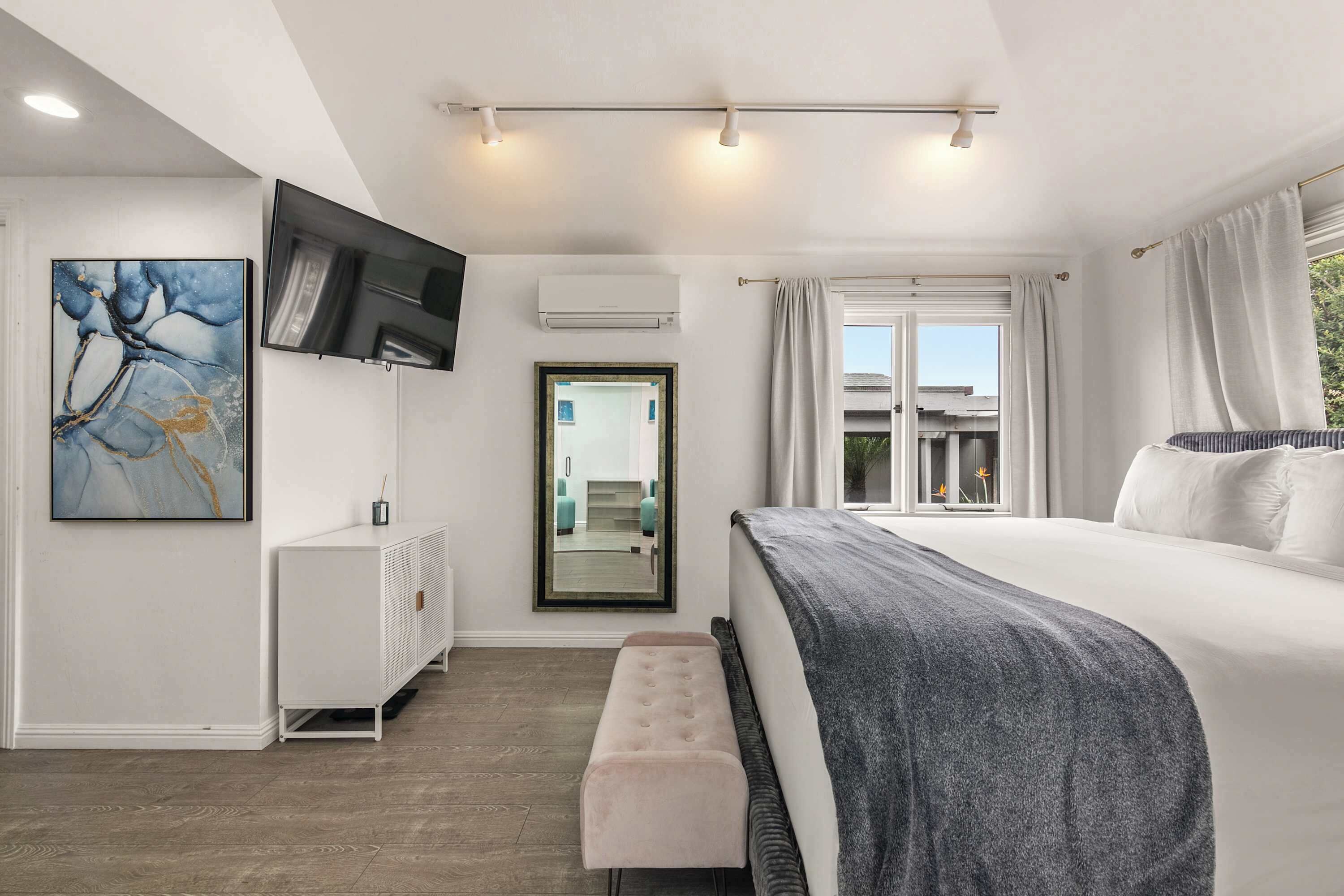 Ein modernes Schlafzimmer mit einem großen Bett, einer Bank, einem Fernseher und einem Fenster mit Vorhängen.