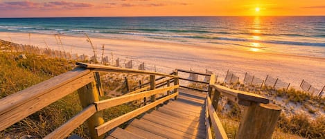 A wooden boardwalk leading to a beach with a sunset in the background.