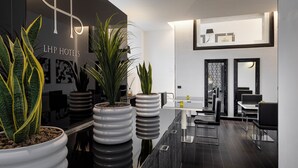 Un hall d’hôtel moderne avec un comptoir d’accueil, des plantes en pot et un espace repas comprenant des chaises noires et une table en verre.