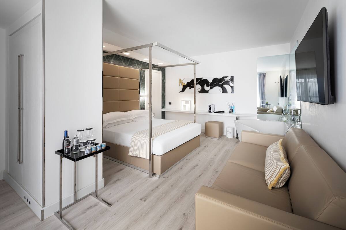 A modern hotel room with a bed, a sofa, a small table, and a TV.