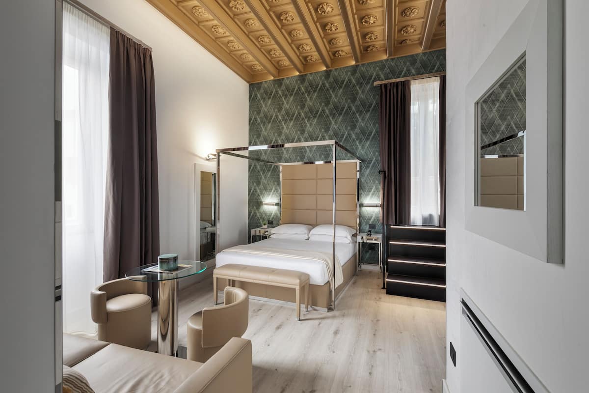 A modern hotel room with a four-poster bed, a sitting area with a glass table, and a large mirror.