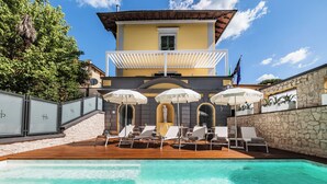 Un espace piscine avec des chaises longues et des parasols, un mur en pierre et un bâtiment doté d’un balcon.