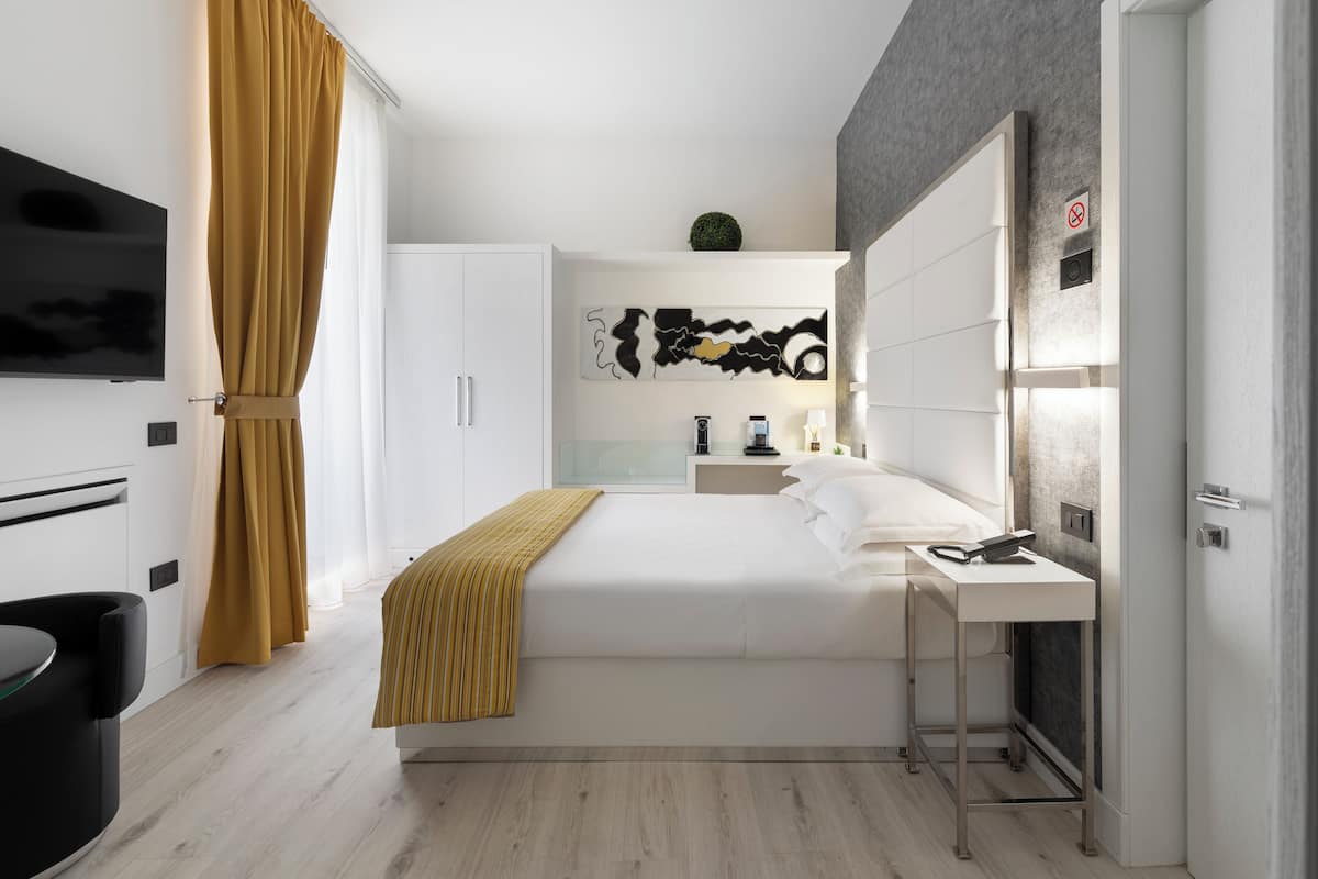 A modern hotel room with a bed, bedside table, and a TV mounted on the wall.