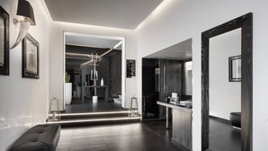 Un hall d’hôtel moderne avec un parquet en bois foncé, un espace salon doté d’un banc, un grand miroir et un comptoir de réception bien éclairé.