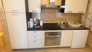 A compact kitchen with white cabinets, a stainless steel range hood, a built-in oven, and a dishwasher. - Apartman Combaj 1 (Crikvenica)