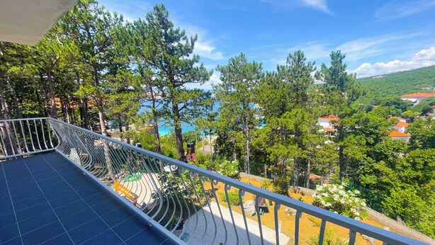 A balcony with a view of a coastal area, trees, and a distant town. - Apartman Combaj 1 (Crikvenica)