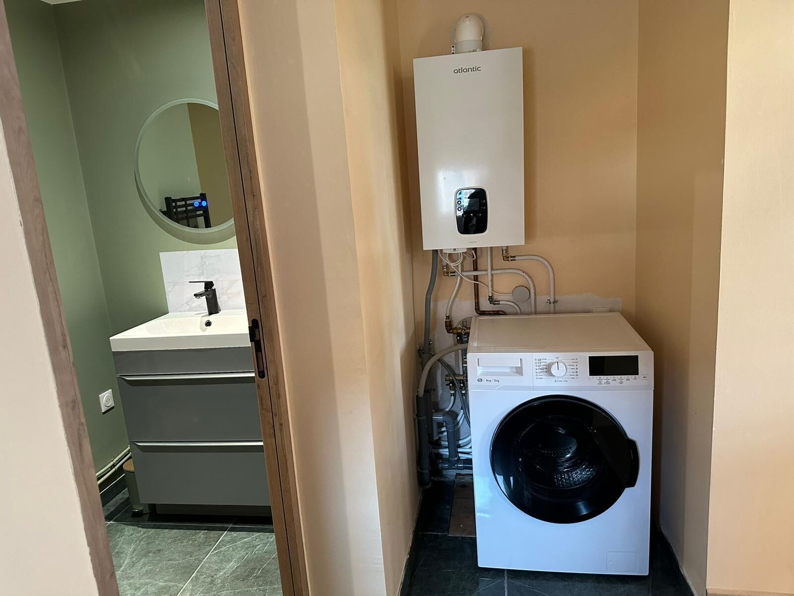 A compact laundry room with a washing machine, a sink, and a water heater.