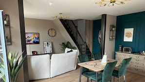A modern dining area with a wooden table and green upholstered chairs, a staircase, and a TV mounted on the wall.