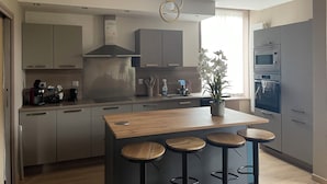 A modern kitchen with a central island, bar stools, stainless steel appliances, and a potted orchid.