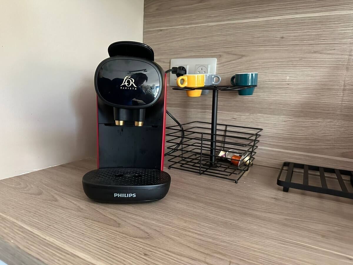 A coffee maker on a wooden surface with a power outlet and a metal rack holding cups in the background.
