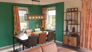 Un comedor con una mesa y sillas de madera, una lámpara colgante y una estantería con objetos decorativos.