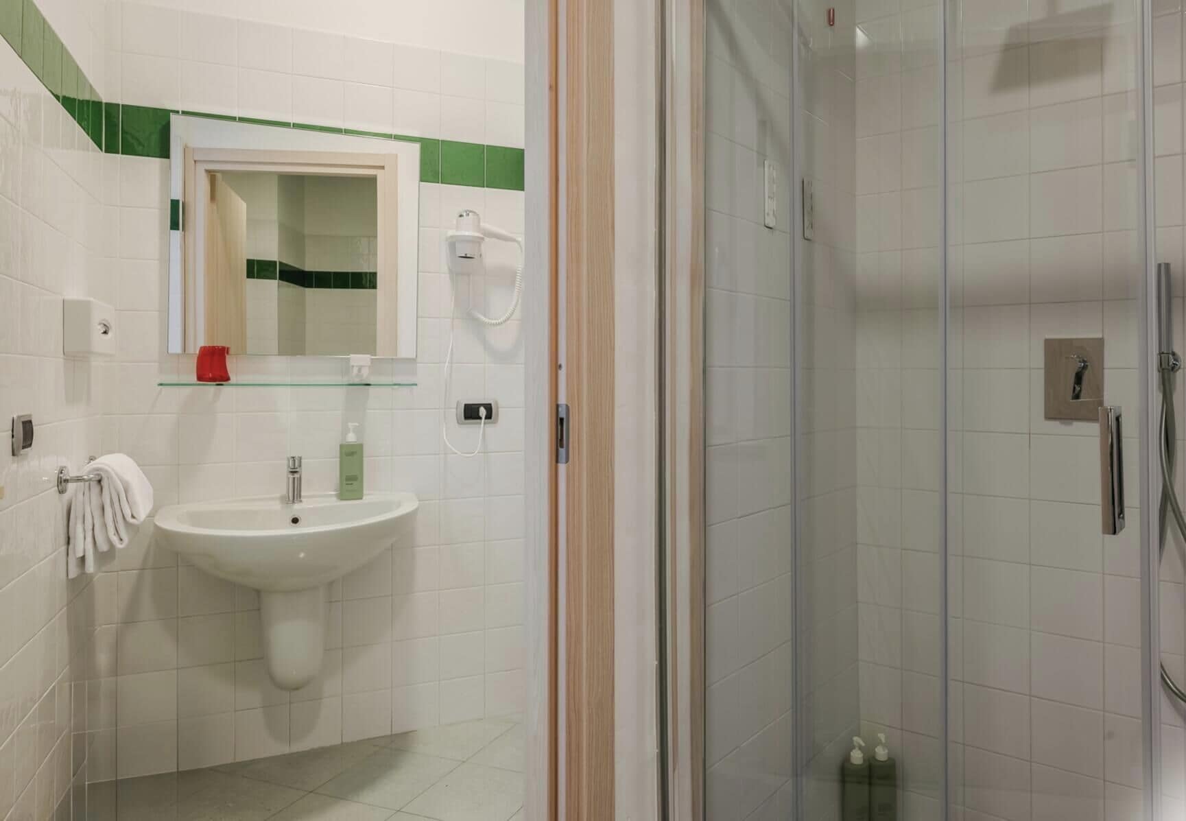 Un baño con un lavamanos blanco, una cabina de ducha con paredes de vidrio y un espejo con una banda verde.