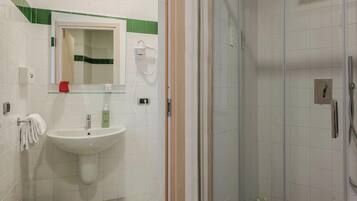 Un baño con un lavamanos blanco, una cabina de ducha con paredes de vidrio y un espejo con una banda verde.