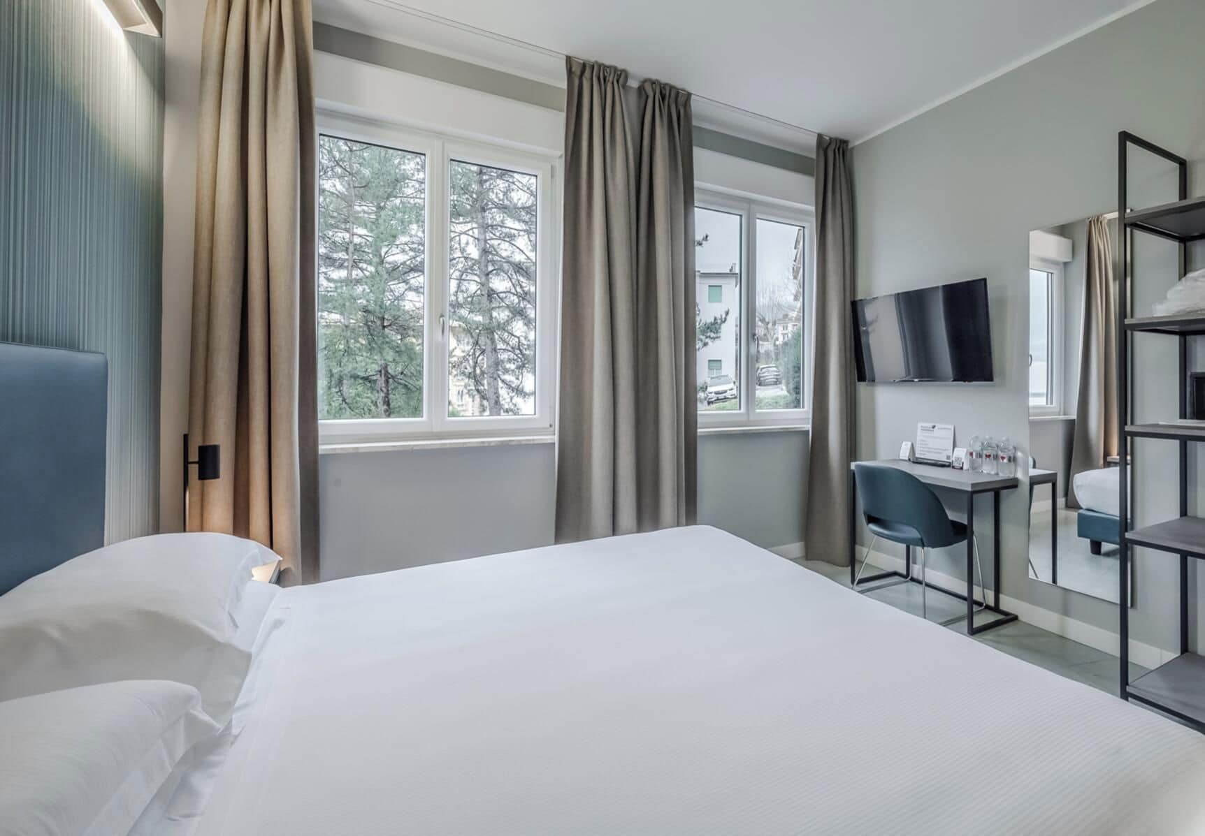 A hotel room with a bed, a desk, a chair, a TV, and a window with curtains.