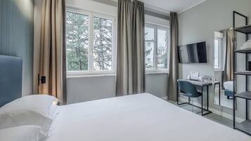 Habitación de hotel con cama, escritorio, silla, televisor y ventana con cortinas.