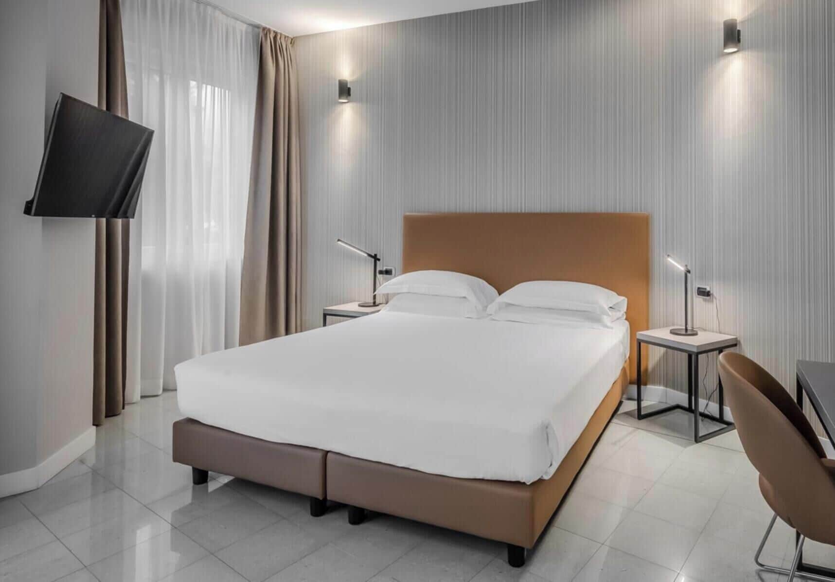 Una camera d'albergo moderna con un letto grande, comodini, una TV a schermo piatto e una poltrona.