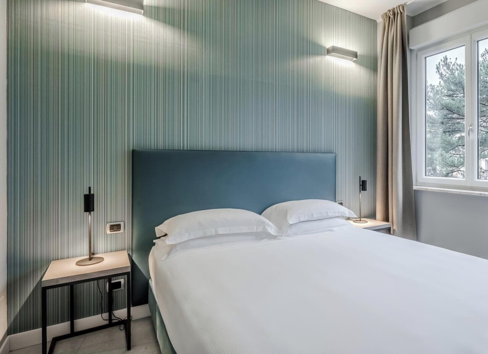 A hotel room with a bed, bedside tables, and a window with a view.