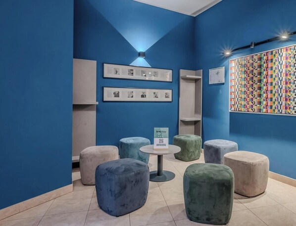 A room with blue walls, multiple seating areas including ottomans and a round table, and framed artwork on the walls. - Hotiday Apartments La Spezia (La Spezia)
