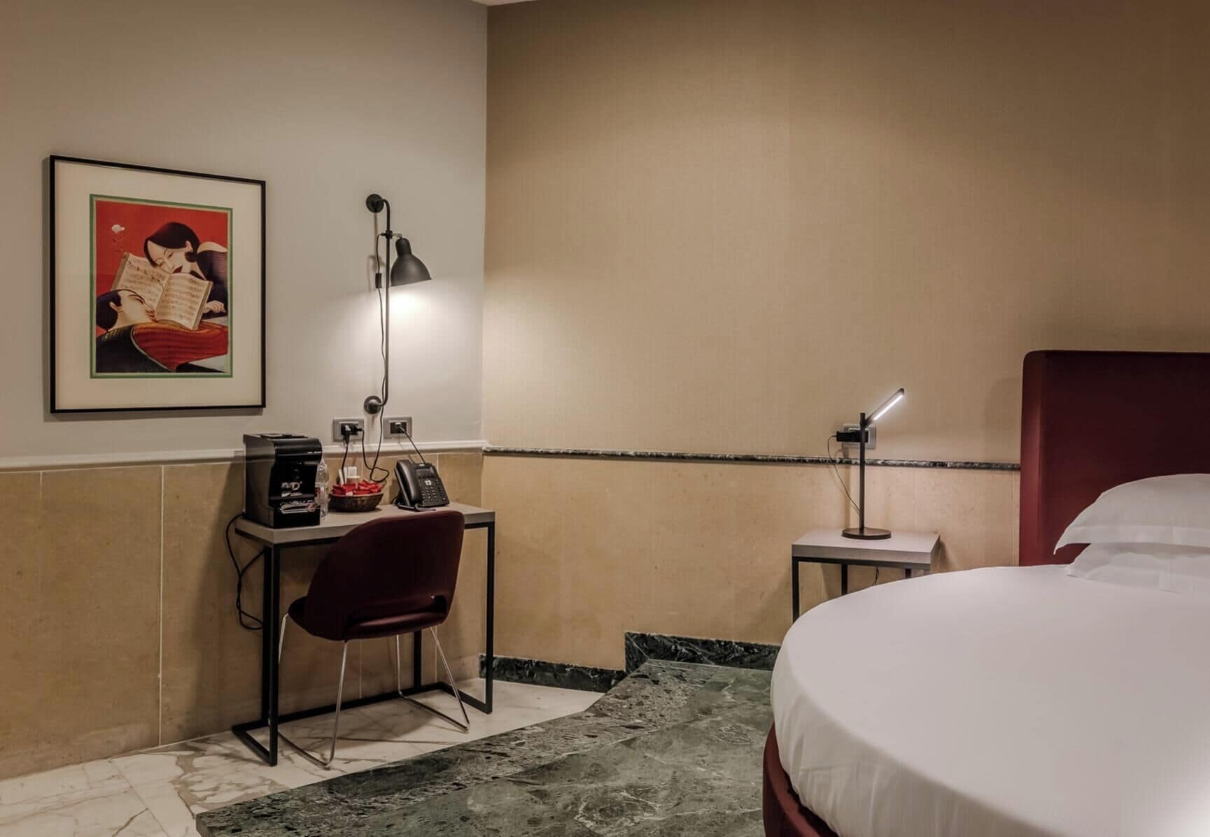 Habitación de hotel con una cama, un escritorio con una silla, una lámpara, un teléfono y un cuadro en la pared.