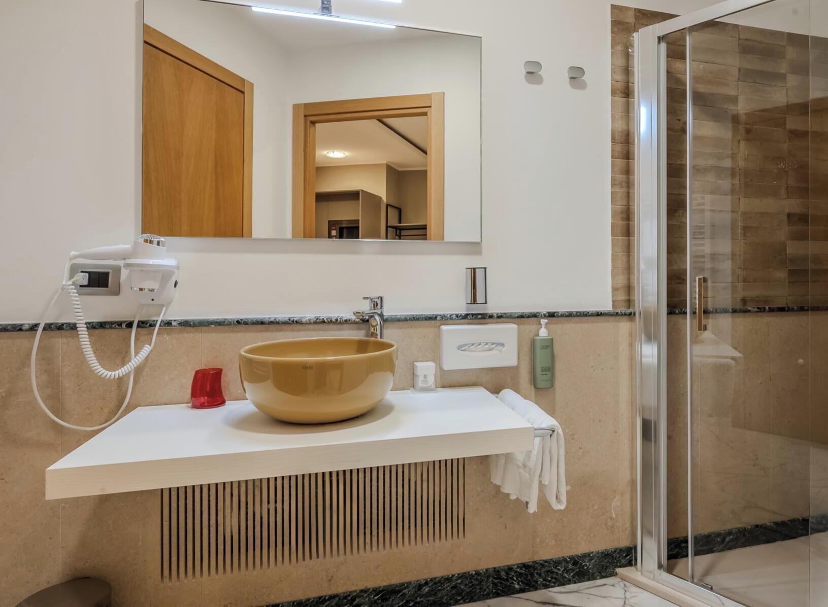 Une salle de bain avec un grand miroir, un lavabo, un sèche-cheveux et un espace douche.