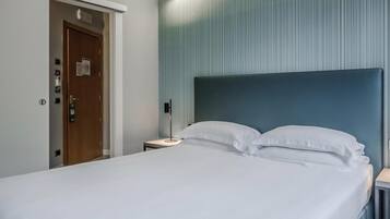 Una camera d'albergo con un letto, un comodino, una porta e un punto luce fissato al muro.