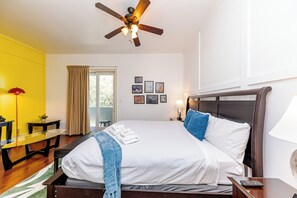 A hotel room with a large bed, a ceiling fan, a desk, and a window with curtains.