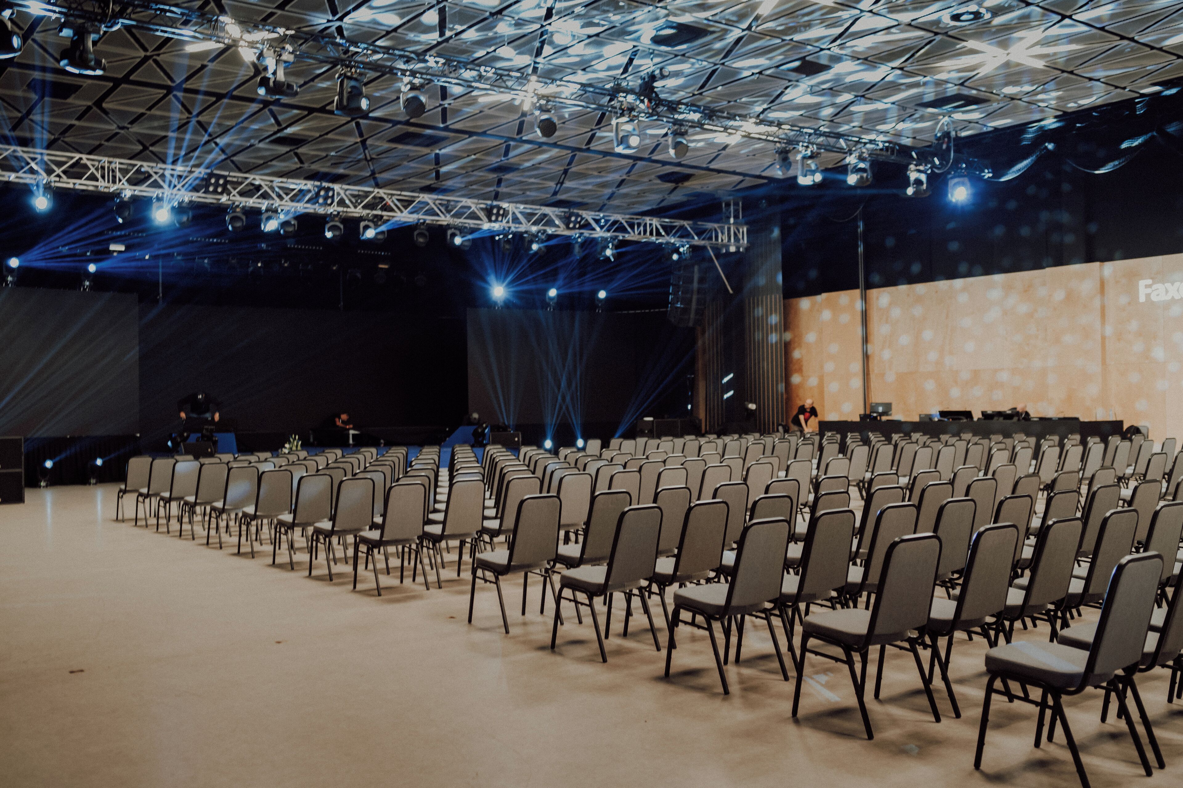 A large indoor auditorium with rows of chairs, a stage with lighting equipment, and a projection screen.