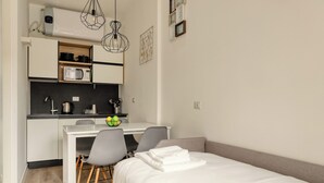 A compact bedroom with a single bed, a small kitchenette, and a desk with chairs.