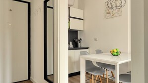 A modern dining area with a white table, grey chairs, and a kitchen area in the background.