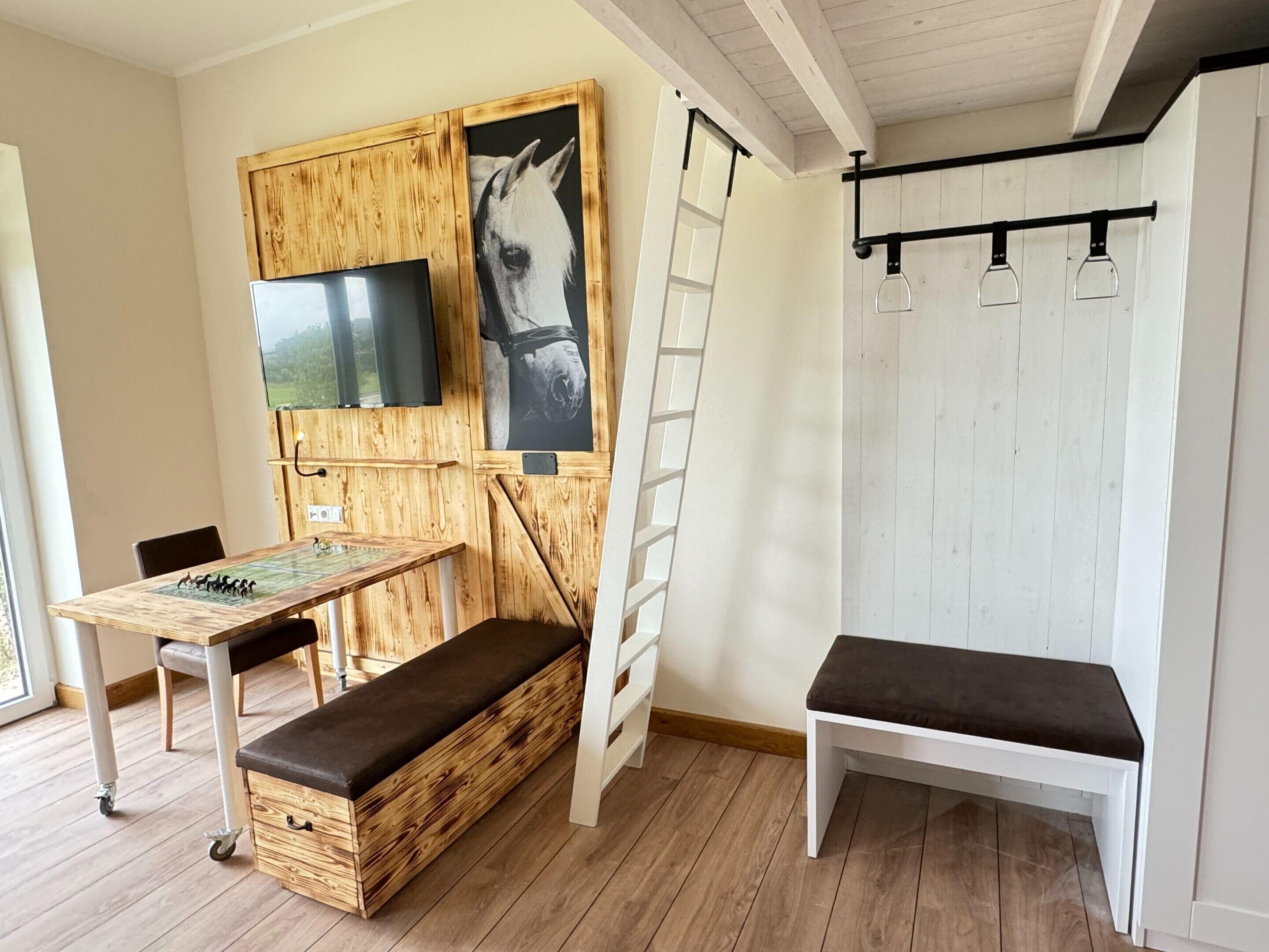 A room with a wooden bench, a table with a chess set, a TV mounted on a wooden panel, and a white wall with a ladder.