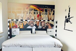 Un dormitorio con cama, cabecera con un mural y un adhesivo de pared de un jugador de fútbol.
