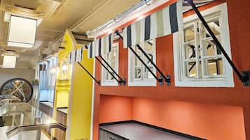 Une chambre d’hôtel avec une cloison en verre, un pilier jaune et des auvents rayés au-dessus des fenêtres.