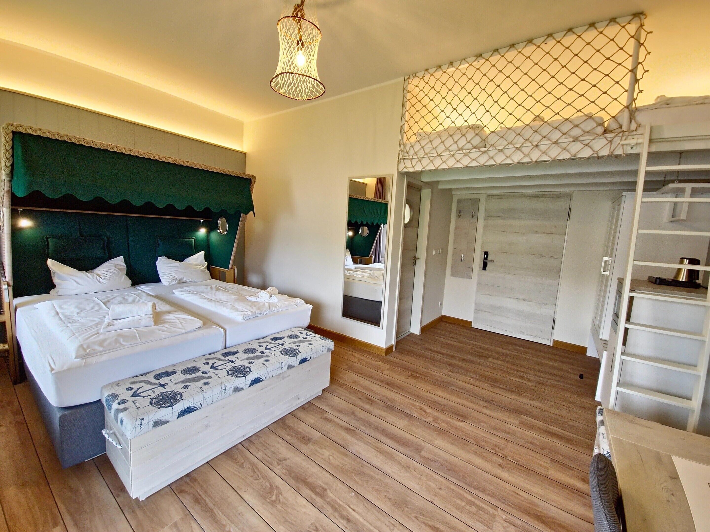 Quarto de hotel com uma cama grande, um banquinho, piso de madeira, espelho e guarda-roupa.