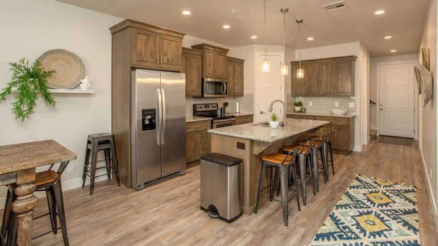 Una cocina moderna con armarios de madera, electrodomésticos de acero inoxidable y una isla central con taburetes de bar.