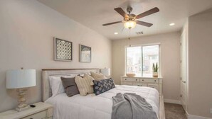 Un dormitorio con cama, mesitas de noche, ventilador de techo y ventana con persianas.